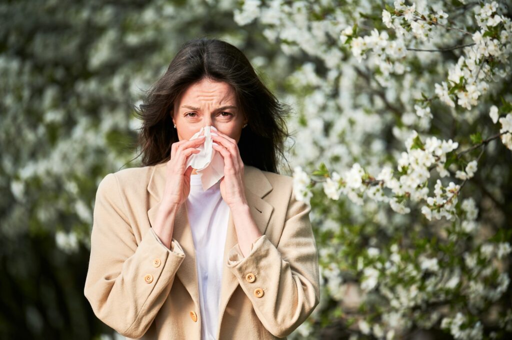 Woman allergic suffering from seasonal allergy at spring, sneezing, blowing nose with handkerchief.